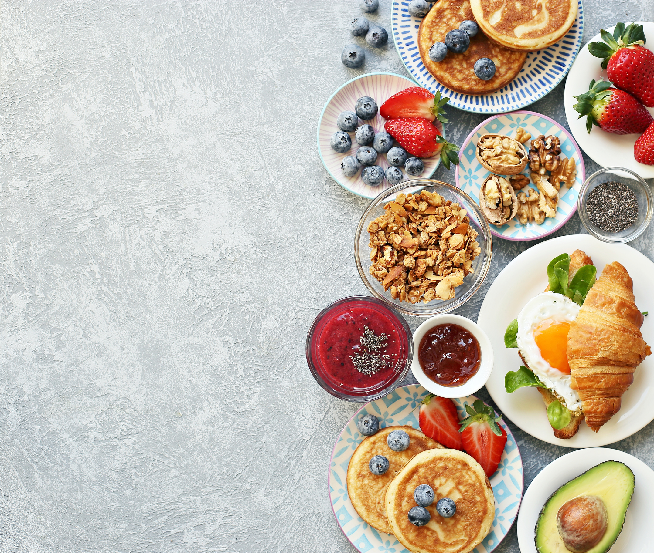 Breakfast food table. Festive brunch set, meal variety with granola, fried egg, pancakes, croissants, smoothie ,fresh vegetables, berries and fruits.